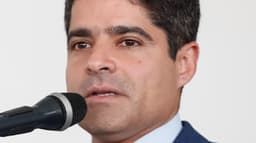 ACM Neto discursa ao microfone em cerimônia pública, de terno azul e gravata