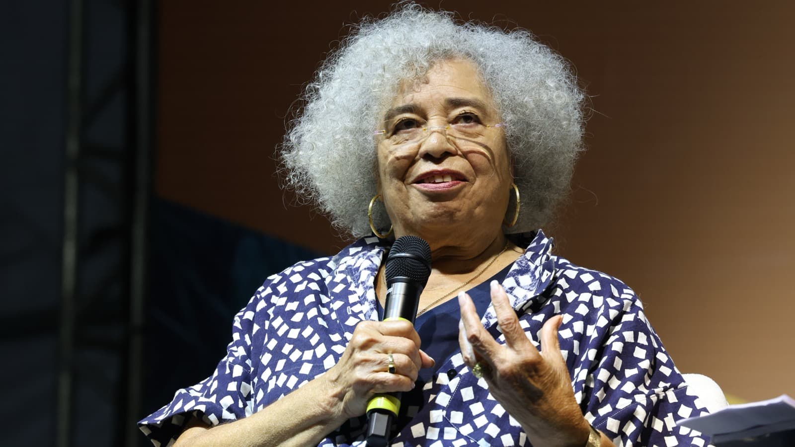 A ativista e filósofa Angela Davis, de cabelo grisalho e camisa azul-marinho estampada, fala ao microfone sentada no palco durante mesa da Flip 2026, em Paraty