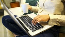 Pessoa navegando na internet em um notebook, segurando uma xícara de café