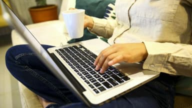 Pessoa navegando na internet em um notebook, segurando uma xícara de café