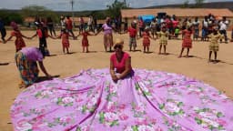 Mulheres e crianças quilombolas em roda durante encontro comunitário, com mulher em vestido tradicional ao centro