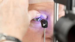 Médico realiza exame oftalmológico em paciente, usando instrumento de avaliação ocular em consultório