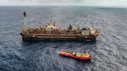 Vista aérea de plataforma FPSO de produção de petróleo no mar, ao lado de embarcação de apoio