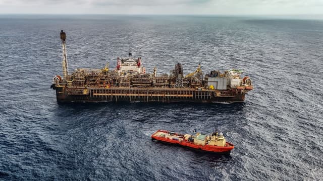 Vista aérea de plataforma FPSO de produção de petróleo no mar, ao lado de embarcação de apoio