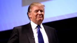 Donald Trump em discurso público, de terno escuro e gravata azul