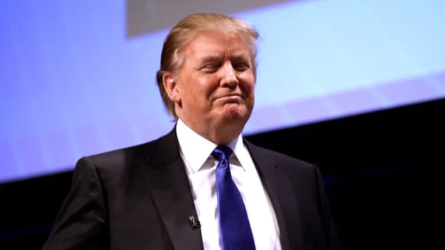 Donald Trump em discurso público, de terno escuro e gravata azul