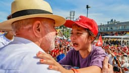 Lula discursa em comício de campanha com bandeiras e multidão ao fundo