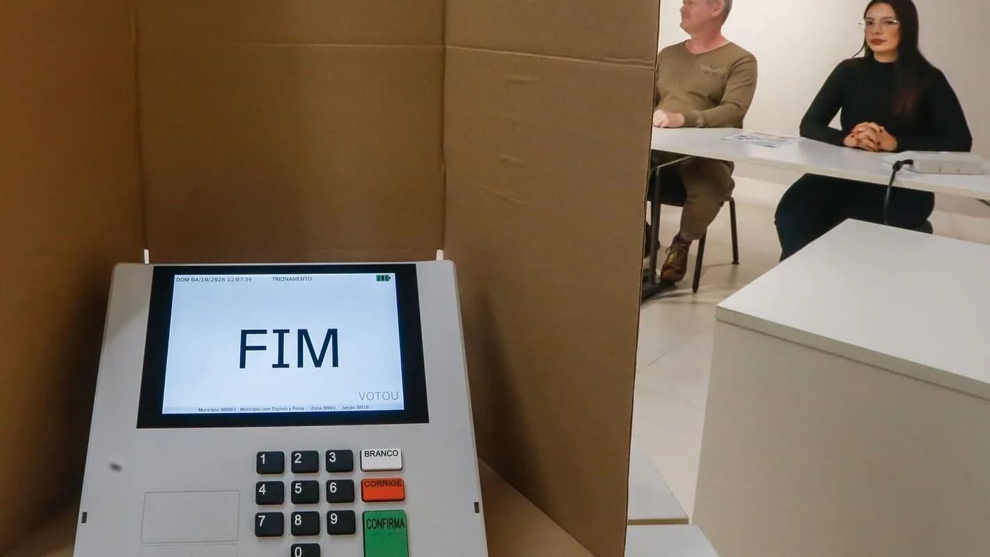 Eleitores numa cabine de votação com urna eletrônica exibindo a palavra FIM