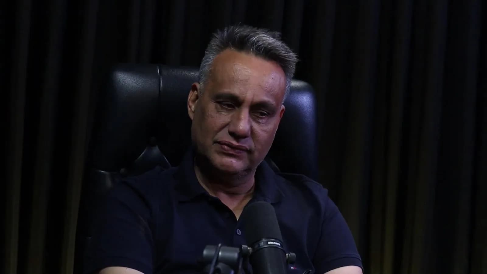 Rogério Furtado fala de forma pausada durante o podcast Encampus, em cadeira de couro preta contra fundo escuro