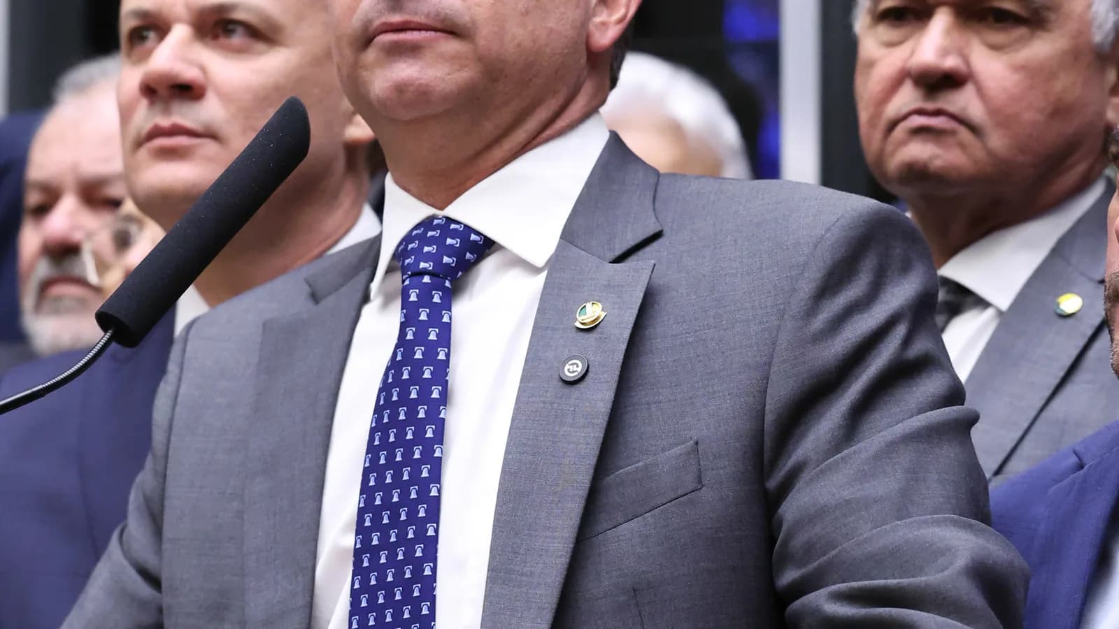 Flávio Bolsonaro no plenário da Câmara, de terno cinza, rodeado por outros parlamentares