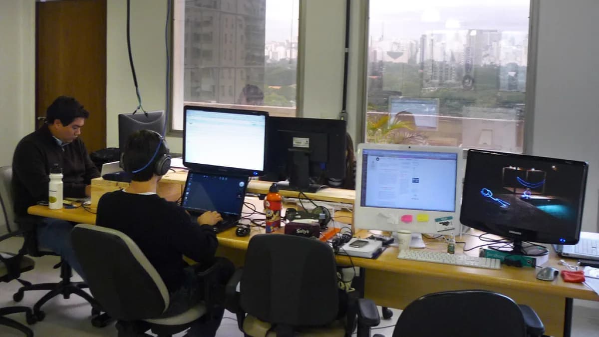 Pessoas trabalhando em mesa com vários computadores em escritório