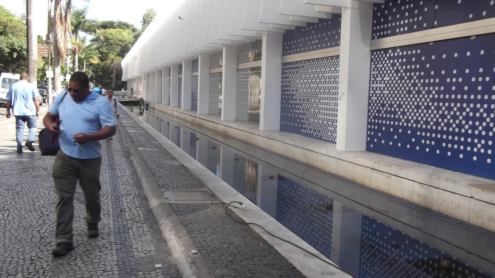 Fachada do Palácio das Artes, em Belo Horizonte, com pedestre caminhando junto ao espelho d'água