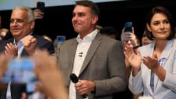 Flávio Bolsonaro recebe apoio de aliados em evento de campanha, cercado por microfones e celulares