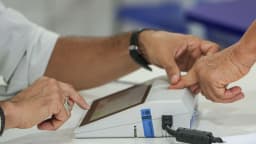 Mãos de eleitor usando leitor biométrico em urna eletrônica durante votação