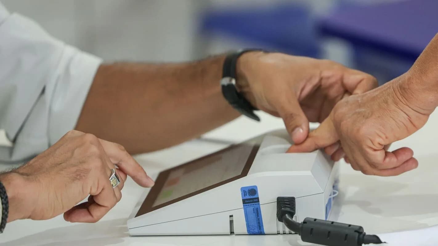 Mãos de eleitor usando leitor biométrico em urna eletrônica durante votação