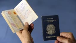 Mãos seguram passaporte brasileiro aberto com carimbos de viagem
