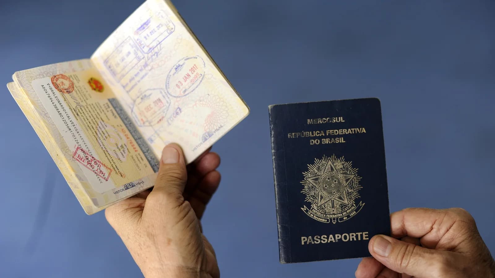 Mãos seguram passaporte brasileiro aberto com carimbos de viagem