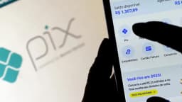 Mão segura celular com aplicativo bancário mostrando menu de empréstimo, cartão e consórcio