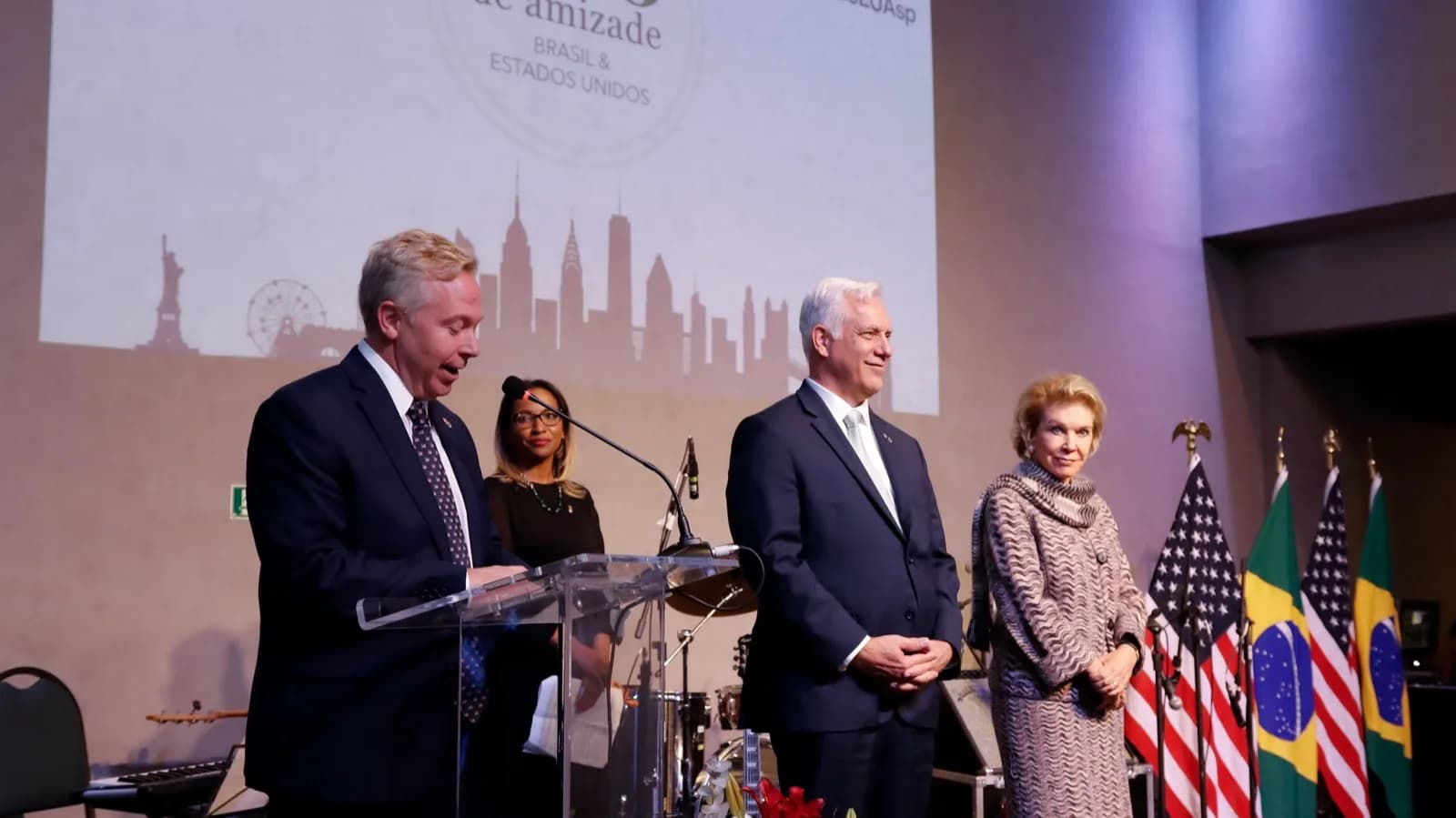 Autoridades americanas discursam em evento do Consulado dos Estados Unidos em São Paulo, com bandeiras do Brasil e dos EUA ao fundo