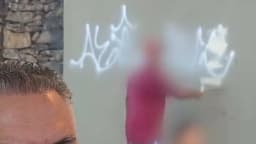 Pessoa com rosto borrado apaga pichação em muro perto do Pontilhão do Horto, em Belo Horizonte, enquanto o prefeito Álvaro Damião aparece em primeiro plano