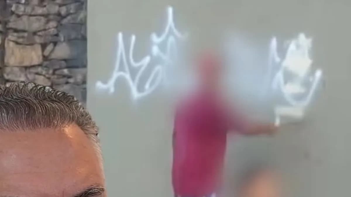 Pessoa com rosto borrado apaga pichação em muro perto do Pontilhão do Horto, em Belo Horizonte, enquanto o prefeito Álvaro Damião aparece em primeiro plano