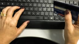 Mão de consumidor digita cartão de crédito em teclado de computador
