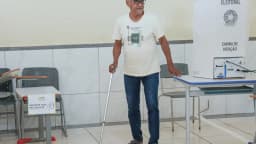 Eleitor idoso em cabine de votação, segurando uma bengala, em seção eleitoral