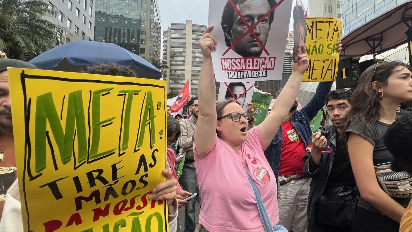 Manifestantes seguram cartazes contra a Meta durante protesto sobre a eleição no Brasil