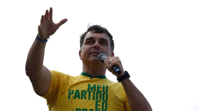 Flávio Bolsonaro de braço levantado segurando microfone durante ato de campanha