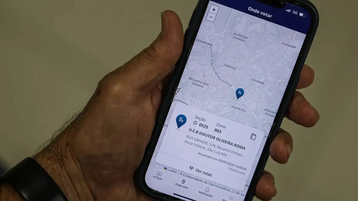 Mão segura celular mostrando o aplicativo e-Título com a localização de uma seção eleitoral