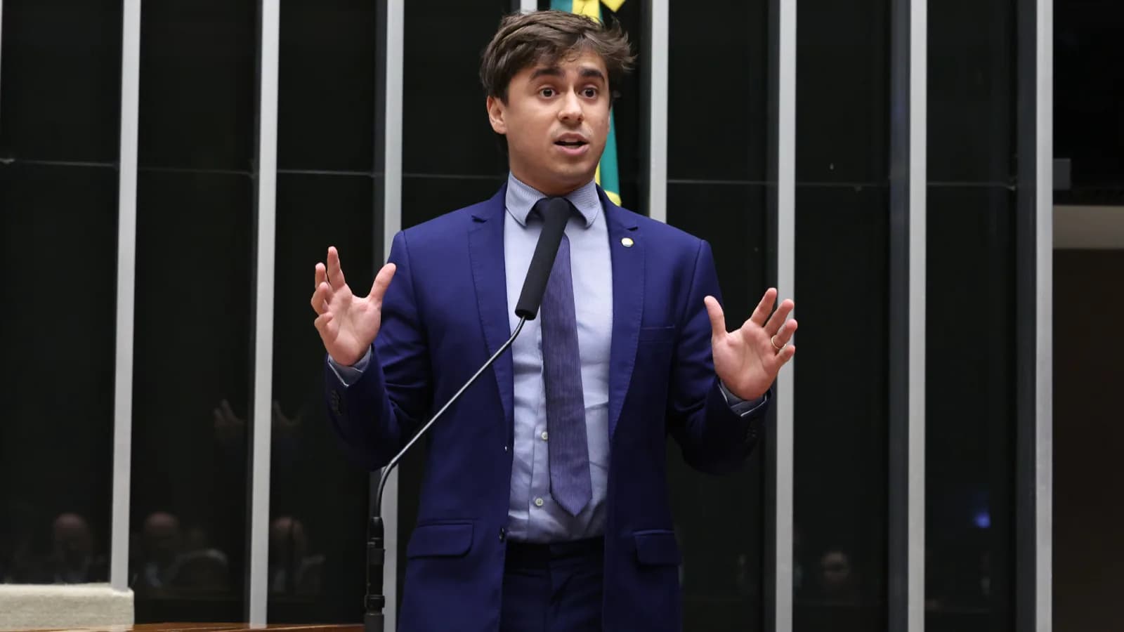 Deputado federal Nikolas Ferreira discursa com as mãos erguidas na tribuna da Câmara dos Deputados