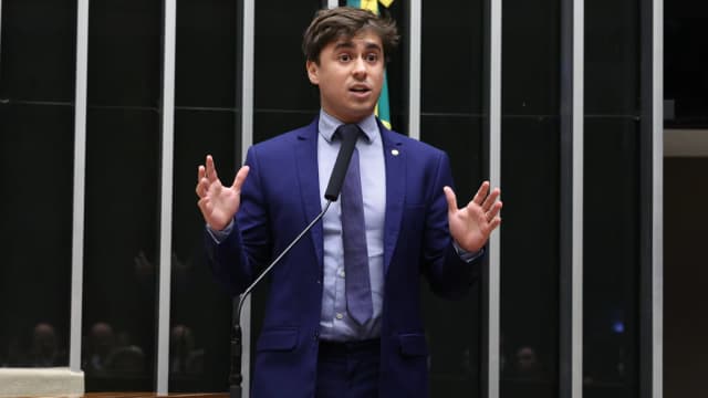 Deputado federal Nikolas Ferreira discursa com as mãos erguidas na tribuna da Câmara dos Deputados
