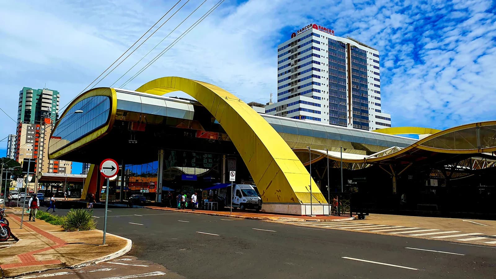 Terminal urbano de Maringá (PR), com arco amarelo e prédios ao fundo, sob céu azul