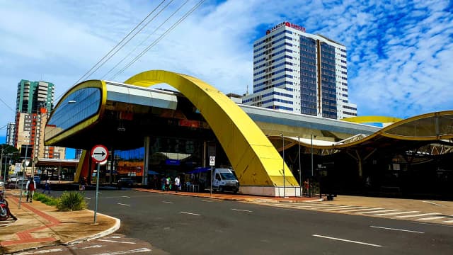 Terminal urbano de Maringá (PR), com arco amarelo e prédios ao fundo, sob céu azul