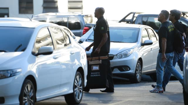 Agentes da Polícia Federal carregam material apreendido durante operação