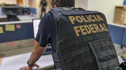 Agente da Polícia Federal de costas durante operação em escritório