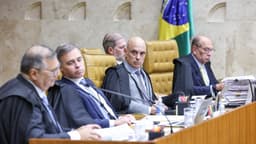 Ministros do Supremo Tribunal Federal, de toga, sentados à bancada durante sessão plenária, com a bandeira do Brasil ao fundo, em imagem de arquivo de abril de 2026