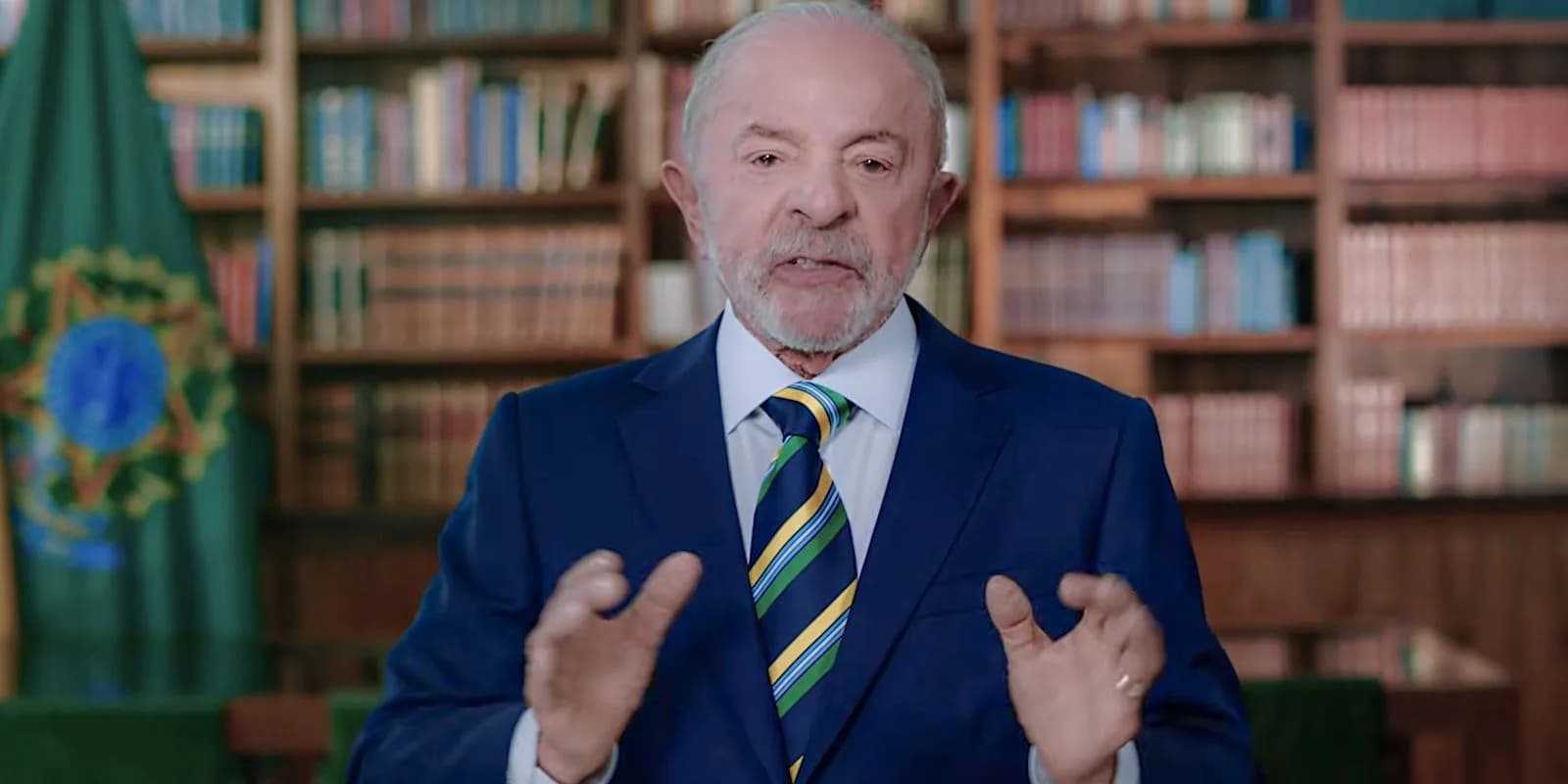 Presidente Lula gesticula durante pronunciamento oficial em cadeia de rádio e TV, ao lado da bandeira do Brasil
