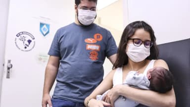 Mãe segura recém-nascido no colo ao lado do pai, em consultório de saúde