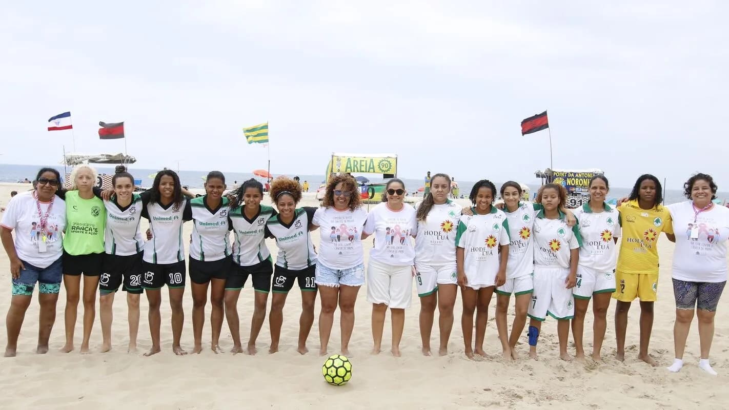 Grupo de mulheres em time de futebol de areia durante ação de conscientização sobre o câncer de mama