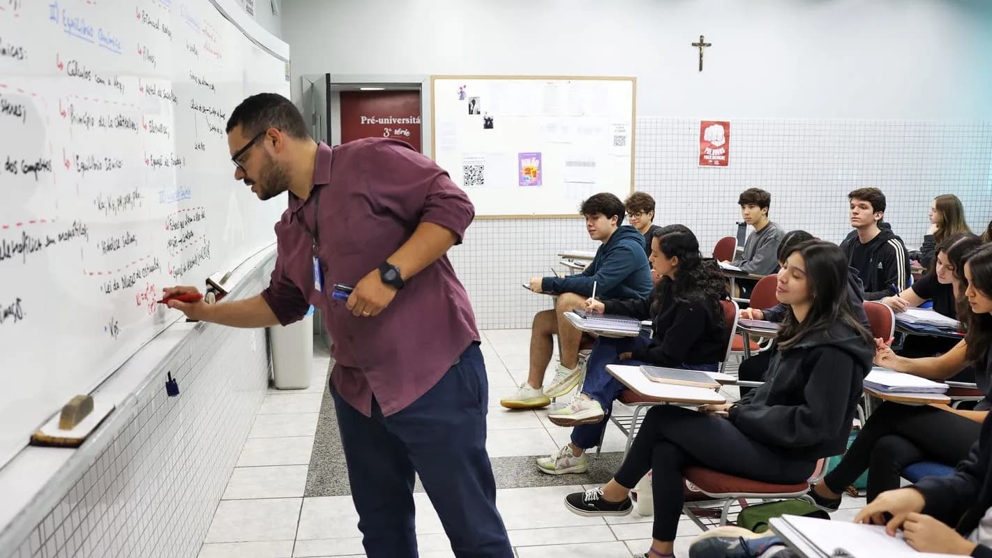 Professor escreve no quadro branco diante de uma turma sentada em carteiras
