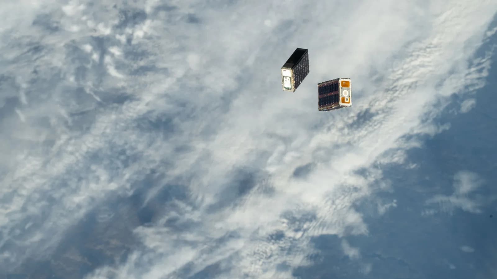 Pequenos satélites são liberados no espaço com a Terra e nuvens ao fundo, vistos a partir da Estação Espacial Internacional