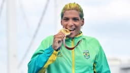 Ana Marcela Cunha sorri e morde medalha de ouro, vestindo agasalho verde do Brasil