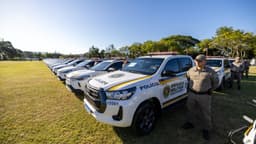 Fileira de viaturas brancas da Brigada Militar do Rio Grande do Sul estacionadas em um campo gramado, com policiais fardados ao lado dos veículos, em imagem de arquivo de março de 2026