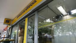 Fachada de agência do Banco do Brasil com um homem ao telefone na entrada
