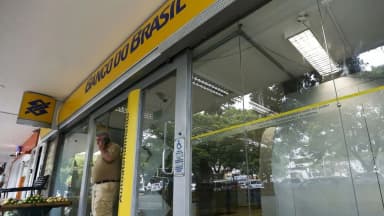 Fachada de agência do Banco do Brasil com um homem ao telefone na entrada