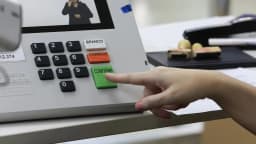 Mão de eleitor aperta o botão confirma em urna eletrônica durante votação