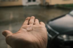 Mão estendida recolhe pedras de granizo durante chuva forte em área urbana