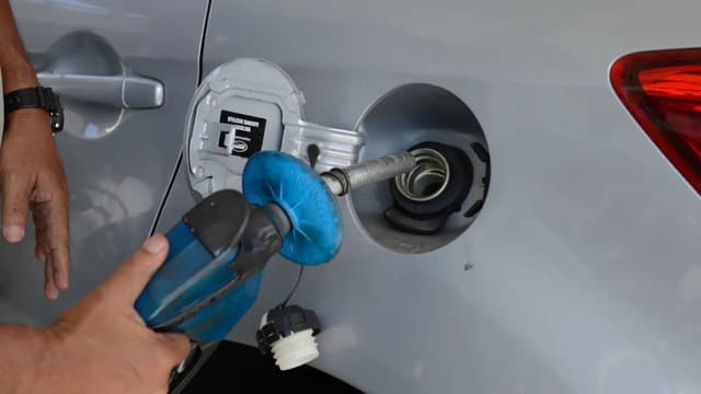 Trabalhador segura a bomba de combustível encaixada no tanque de um carro prata em um posto, em foto de arquivo
