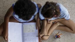 Crianças desenham e escrevem em escola pública, tema ligado às políticas de direitos humanos de Lula e Flávio